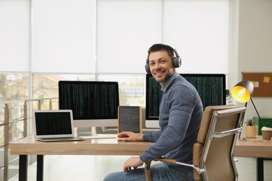 Happy programmer with headphones working at desk in office