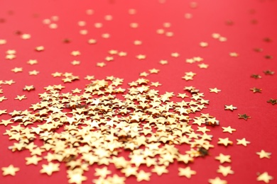 Gold confetti stars on red background, closeup. Christmas celebration