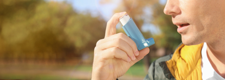 Image of Closeup view of man using asthma inhaler outdoors, space for text. Banner design