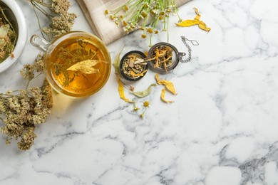 Freshly brewed tea and dried herbs on white marble table, flat lay. Space for text