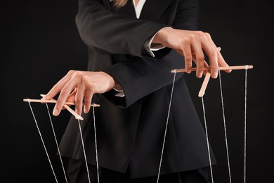 Woman in suit pulling strings of puppet on black background, closeup