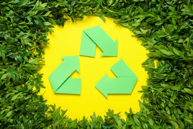Recycling symbol and branches of green plant on yellow background, flat lay