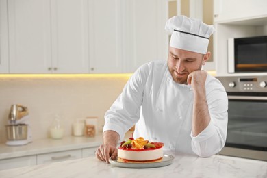 Photo of Happy professional confectioner with delicious cake at table in kitchen