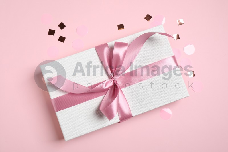 Beautiful gift box and confetti on pink background, flat lay