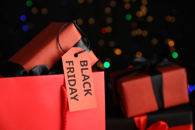 Gift box with Black Friday tag against blurred lights, closeup