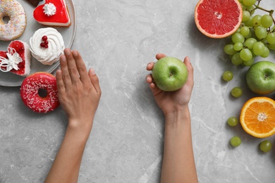 Photo of Concept of choice. Top view of woman holding apple at grey table, closeup