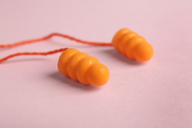 Pair of orange ear plugs with cord on pink background, closeup