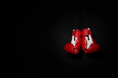 Pair of red boxing gloves hanging on black background, space for text