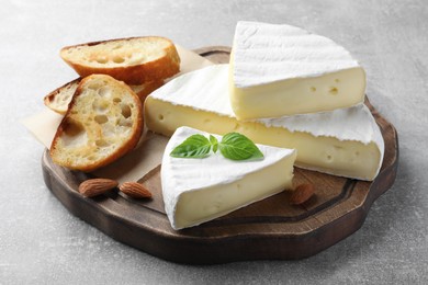 Tasty brie cheese with basil, bread and almonds on grey table