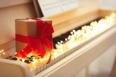 Gift box and fairy lights on piano keys, space for text. Christmas music