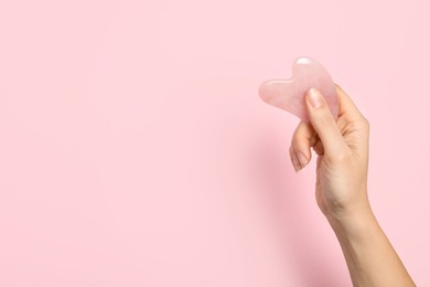 Photo of Woman with rose quartz gua sha tool on light pink background, closeup. Space for text