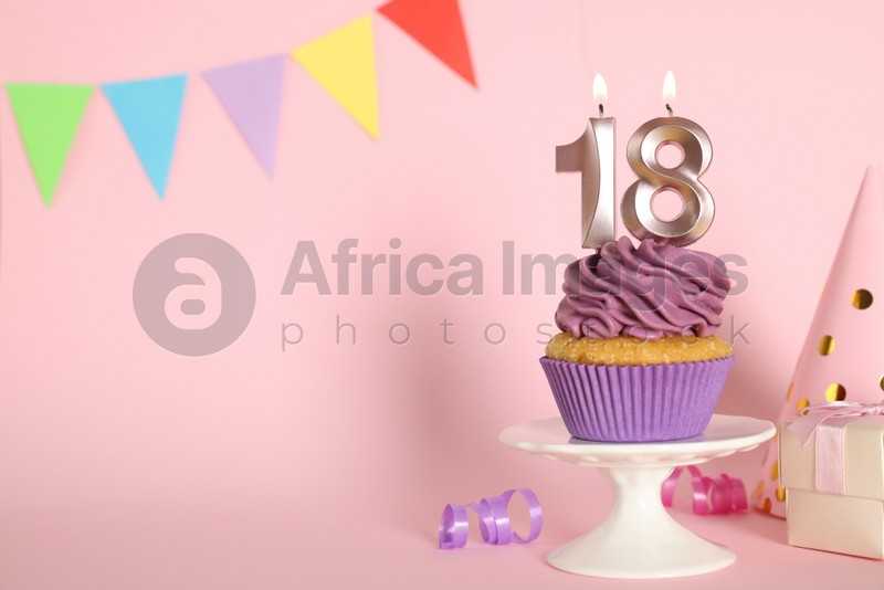 Delicious cupcake with number shaped candles on pink background, space for text. Coming of age party - 18th birthday