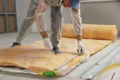 Photo of Worker measuring and cutting insulation material indoors