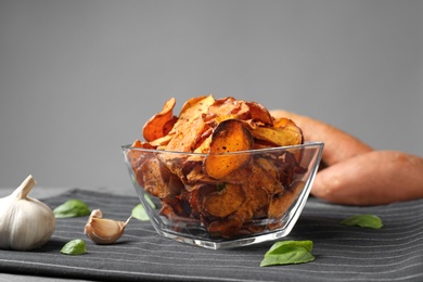Bowl of sweet potato chips and garlic on table against grey background