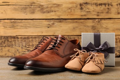 Photo of Happy Father's Day. Shoes for dad and child near gift box on wooden background