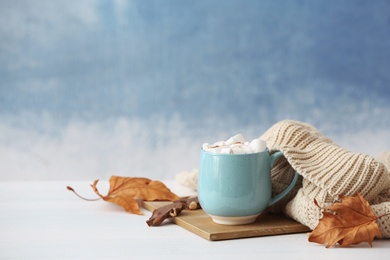 Composition with hot cozy drink in cup and autumn clothing on table