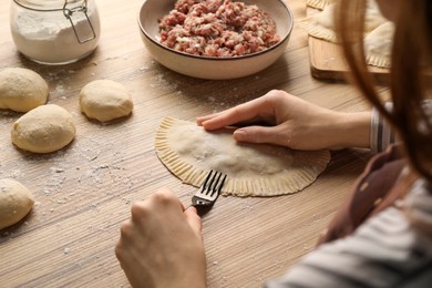Photo of Woman making chebureki with tasty filling at wooden table, closeup