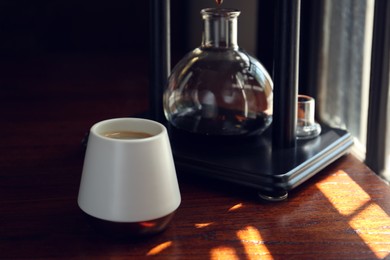 Cup with coffee and vacuum maker on wooden table in cafe