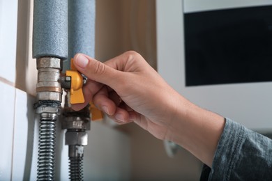 Photo of Woman turning on valve of gas boiler indoors, closeup