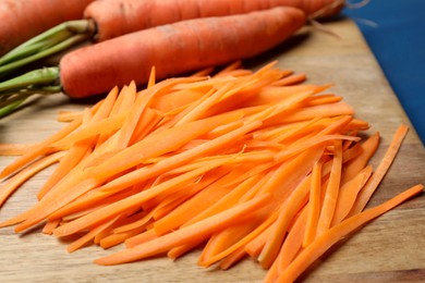 Fresh ripe juicy carrot sticks and whole vegetables on wooden board, closeup