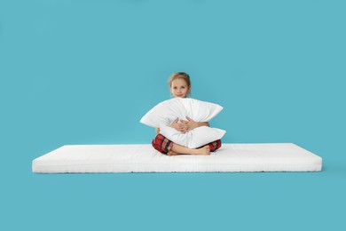 Photo of Little girl hugging pillow on mattress against light blue background