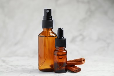 Photo of Bottles of organic cosmetic products and cinnamon sticks on grey marbled background