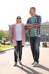 Photo of Mature man helping blind person with long cane walking outdoors