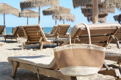 Straw bag on wooden sunbed near sea. Beach accessory