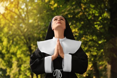 Young nun with hands clasped together praying in park