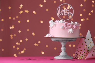 Beautifully decorated birthday cake on pink table against blurred festive lights, space for text
