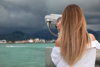 Photo of Woman looking through mounted binoculars at mountains. Space for text