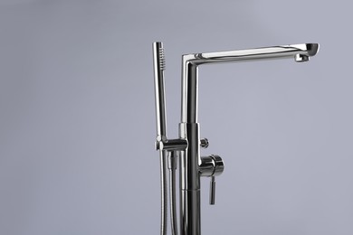 Modern bathtub faucet with hand shower on grey background