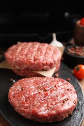 Raw hamburger patties with pepper on black board, closeup