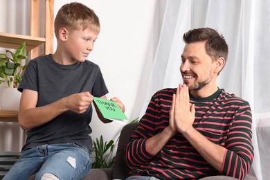 Photo of Happy man receiving greeting card from his son at home