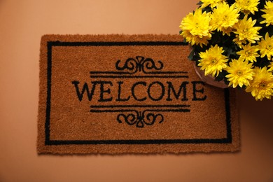 Photo of Doormat with word Welcome and flowers on brown background, flat lay