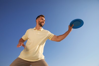 Happy man catching flying disk against blue sky on sunny day, low angle view