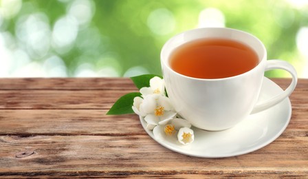 Cup of jasmine tea and fresh flowers on wooden table outdoors, space for text. Banner design