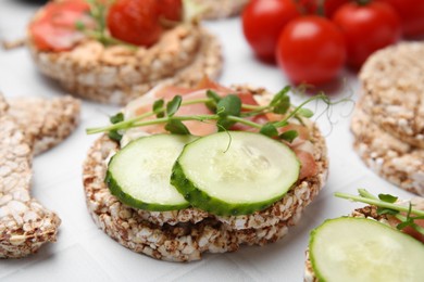 Crunchy buckwheat cakes with prosciutto, cucumber slices and greens on white table, closeup