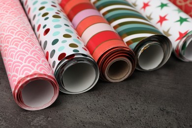 Different colorful wrapping paper rolls on grey table, closeup