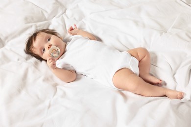 Photo of Cute little baby with pacifier lying on bed