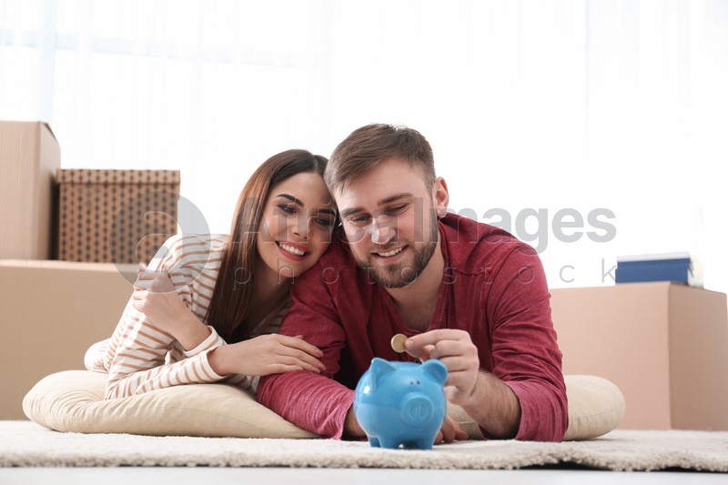 Beautiful young couple with piggy bank and money on floor at home