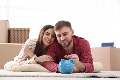 Beautiful young couple with piggy bank and money on floor at home