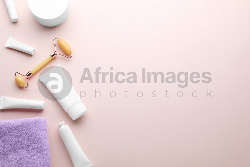Natural face roller, cosmetic products and towel on pink background, flat lay. Space for text