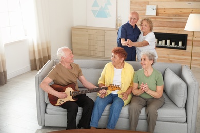 Elderly man playing guitar for his friends in living room