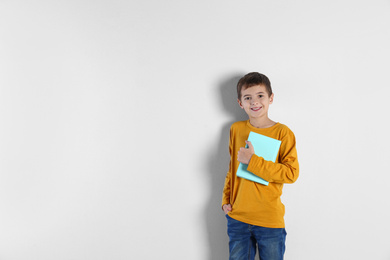 Cute little boy with book on light background, space for text