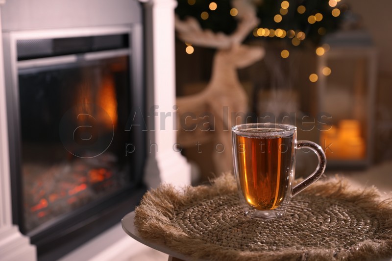 Photo of Glass of hot drink near fireplace in room. Space for text