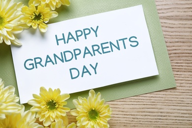 Beautiful yellow flowers and card with phrase Happy Grandparents Day on wooden background, flat lay