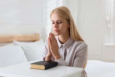 Religious young woman with Bible praying in bedroom