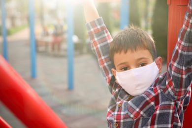 Little boy with medical face mask on playground during covid-19 quarantine