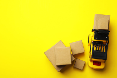 Top view of toy forklift with boxes on yellow background, space for text. Logistics and wholesale concept